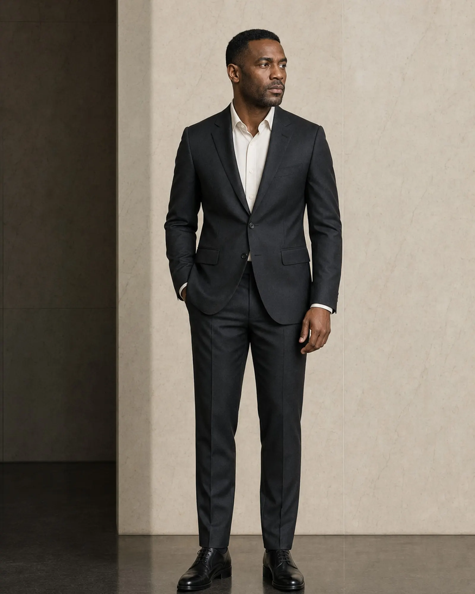 DEMO — Homme debout en costume anthracite, mur de pierre